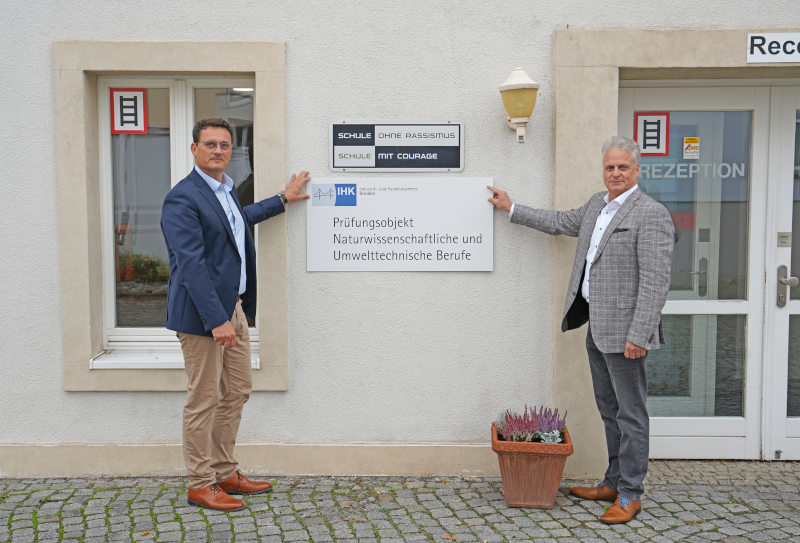 René Günthel (links) und Torsten Köhler präsentieren den Standort des IHK-Prüfungsstandort-Schilds am Eingangsbereich des SBG-Firmengeländes